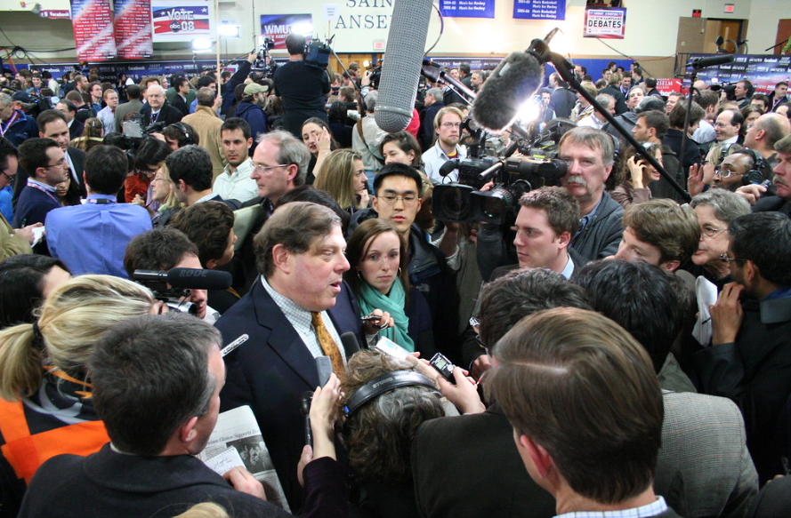 man in a crowd talking to a bank of reporters