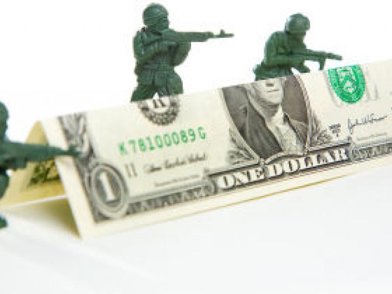 Toy soldiers hiding behind dollar bill